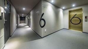 A modern hallway with a number '6' sign, an elevator, and a corridor leading to rooms. - Boutique Hotel HAVE (Busan)