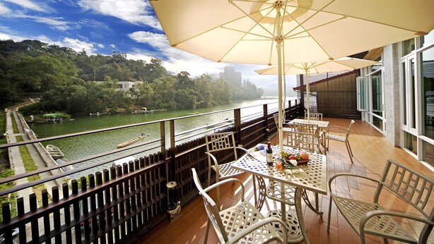 Un balcón con mobiliario exterior, una sombrilla grande y vistas a un río y vegetación.