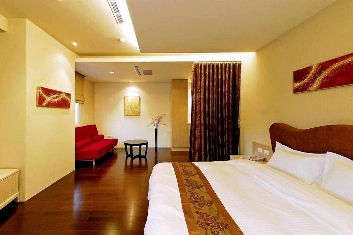 Une chambre d’hôtel avec un lit, un fauteuil rouge, une petite table et un rideau.