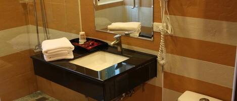 Un baño con ducha envuelta en vidrio, tocador negro con lavamanos, inodoro y toallero con toallas.