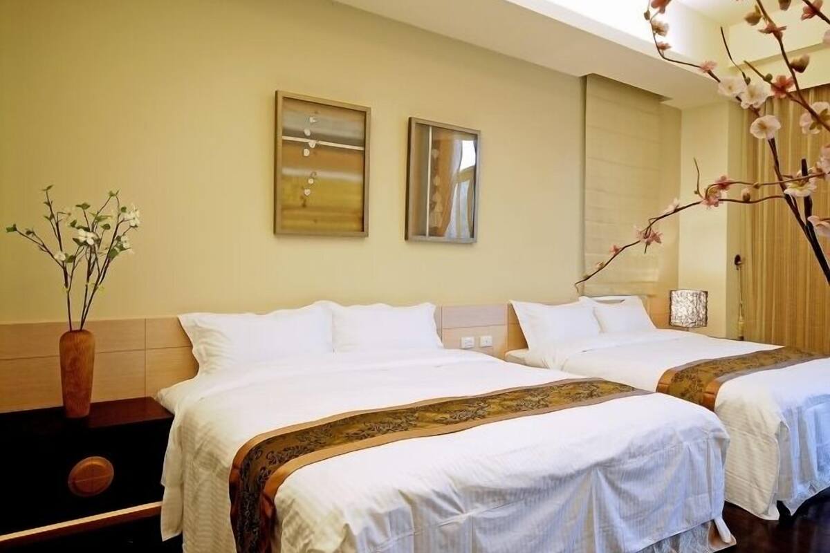 Une chambre d’hôtel avec deux lits, un vase de fleurs et deux œuvres d’art encadrées au mur.