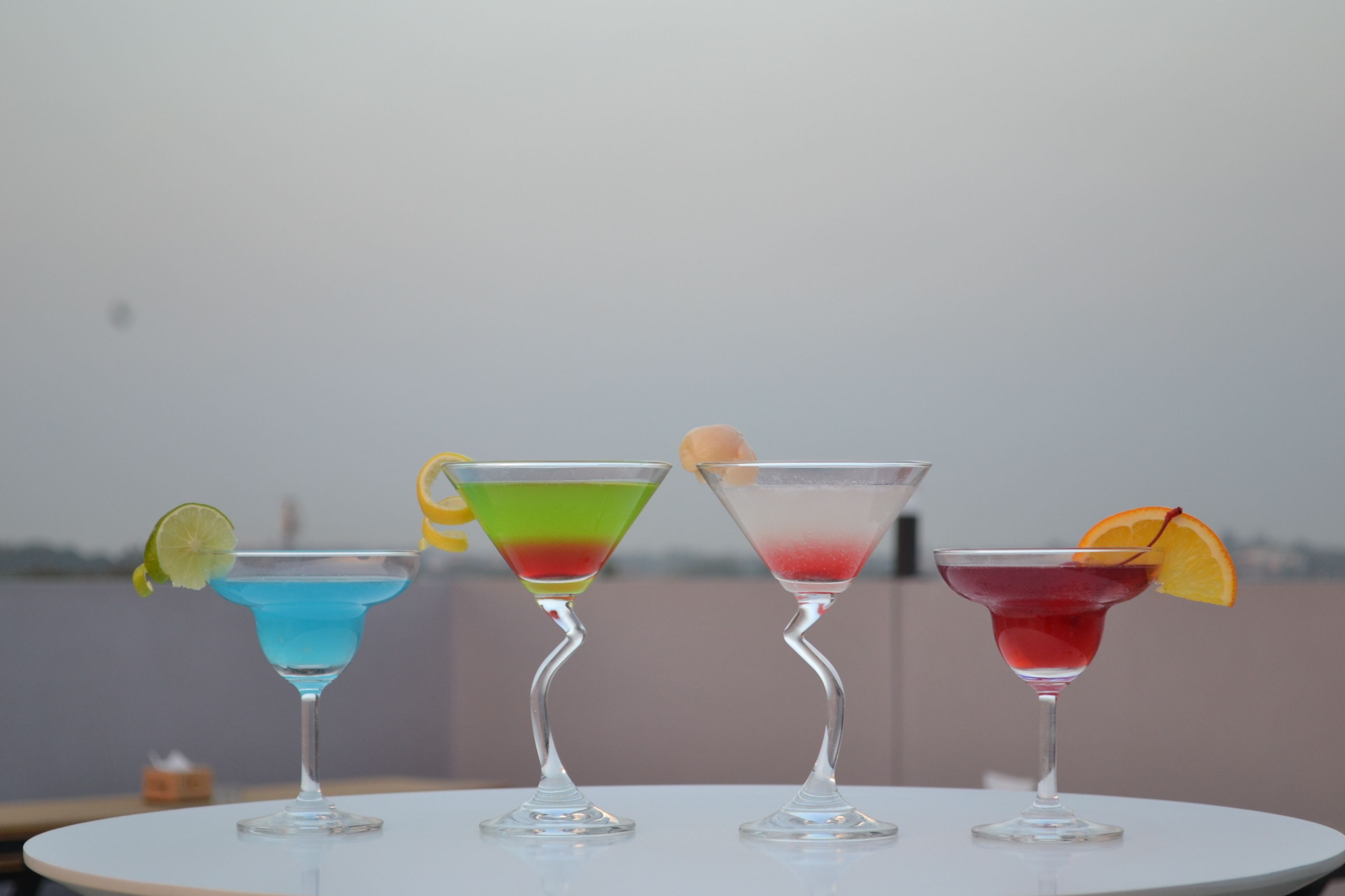 Cuatro vasos de martini con bebidas de colores distintos sobre una mesa blanca.
