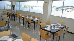 Un comedor amplio con varias mesas y sillas, ventanas grandes con persianas y un diseño limpio y moderno.