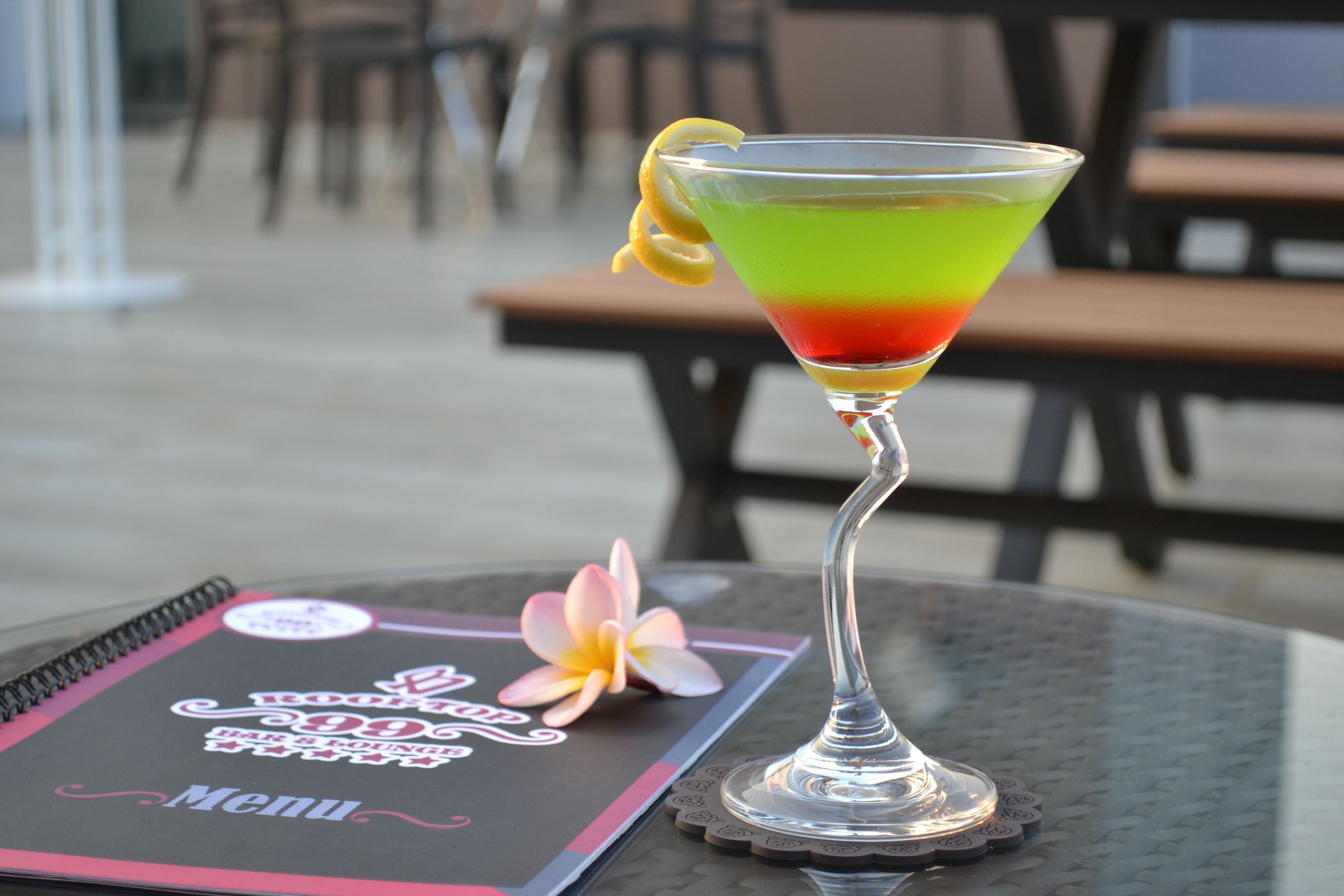 Una copa de martini con una bebida degradada sobre una mesa, un menú y una flor.