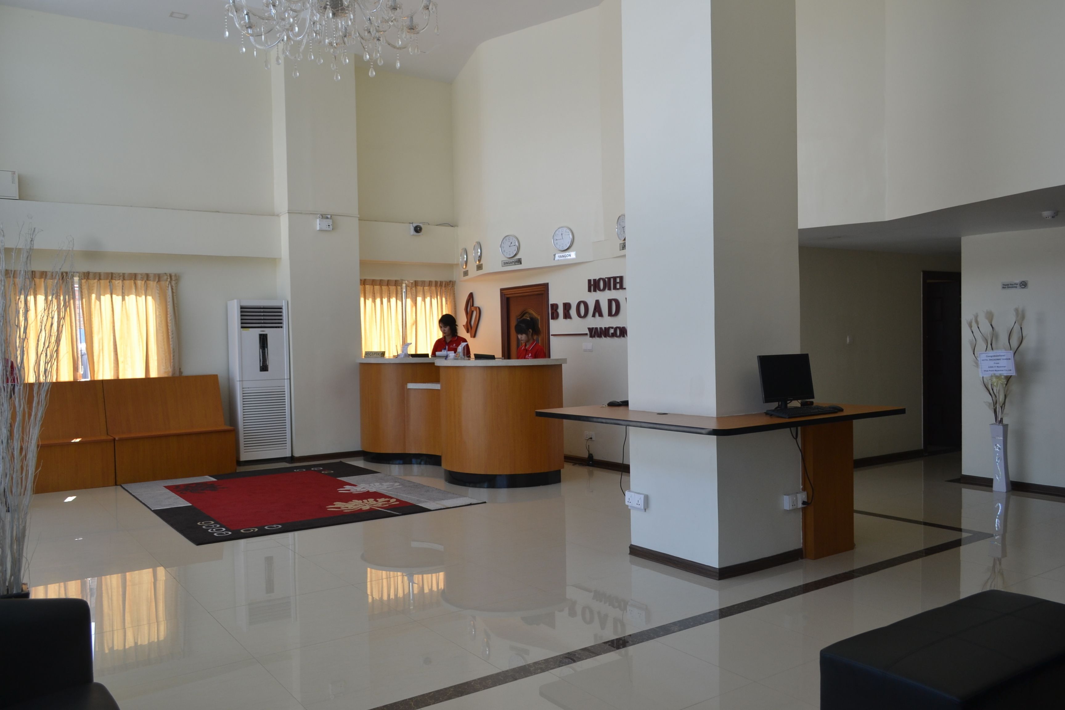 A hotel lobby with a reception desk, a large red rug, and a chandelier.