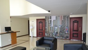 Un hall con mostrador de recepción, dos sofás de cuero negro, una mesa de centro de vidrio y un mural con vistas a la ciudad.