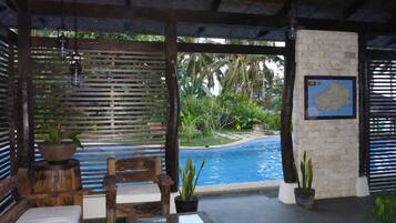 A poolside area with wooden furniture, a stone wall with a map, and a view of a tropical garden.