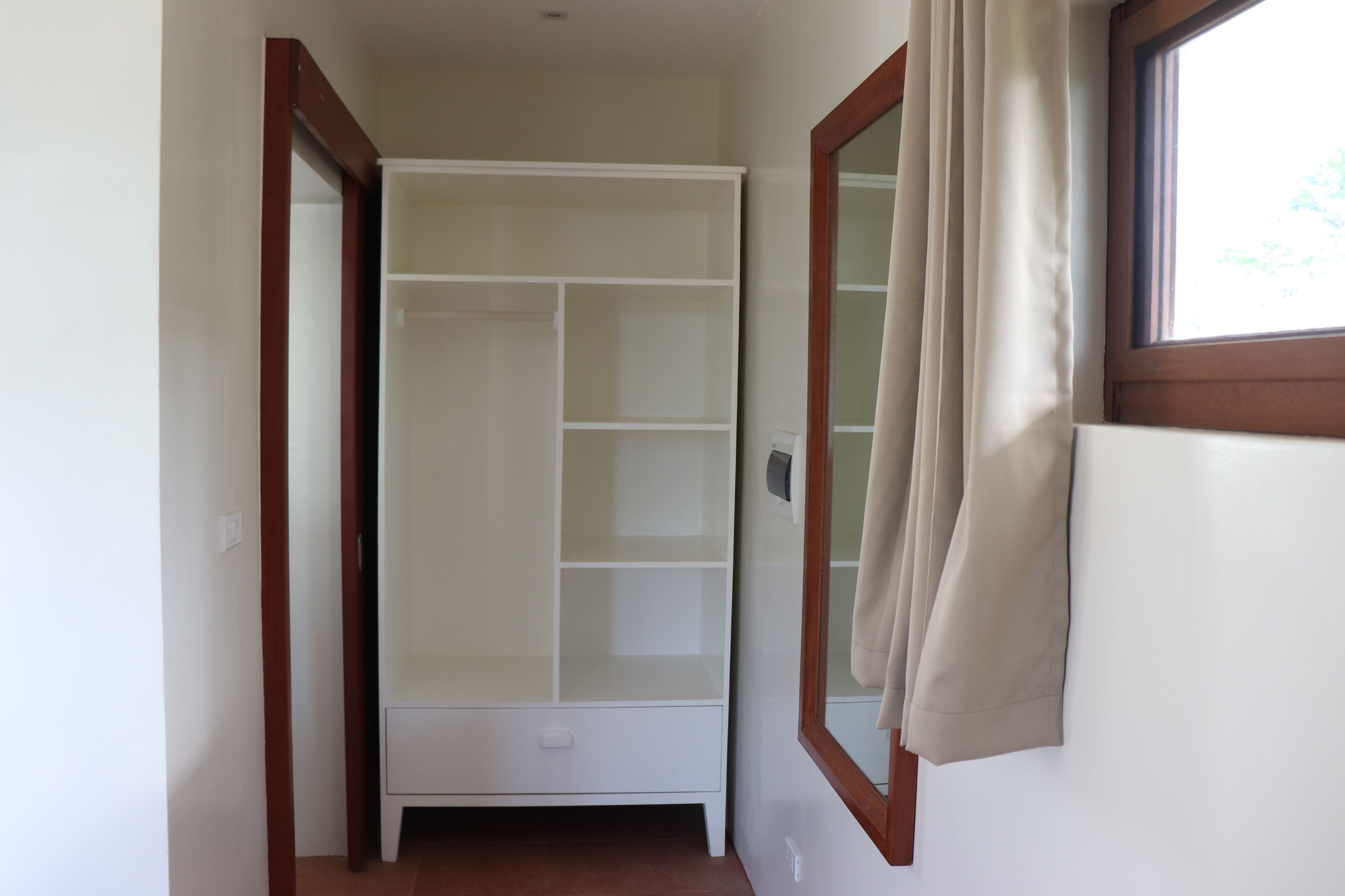 A hallway with a white wardrobe, a wooden door frame, and a window with curtains.