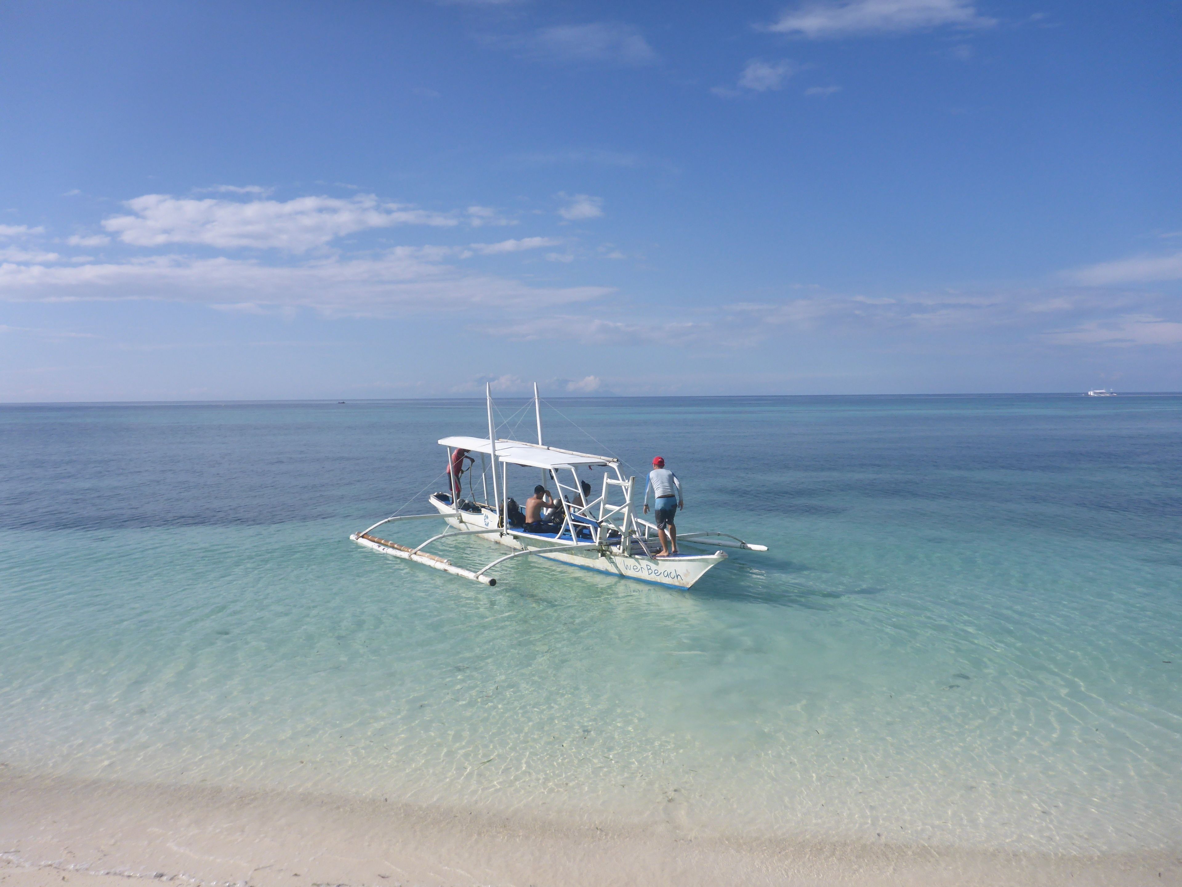 A boat on clear turquoise water with a sandy beach in the foreground.
