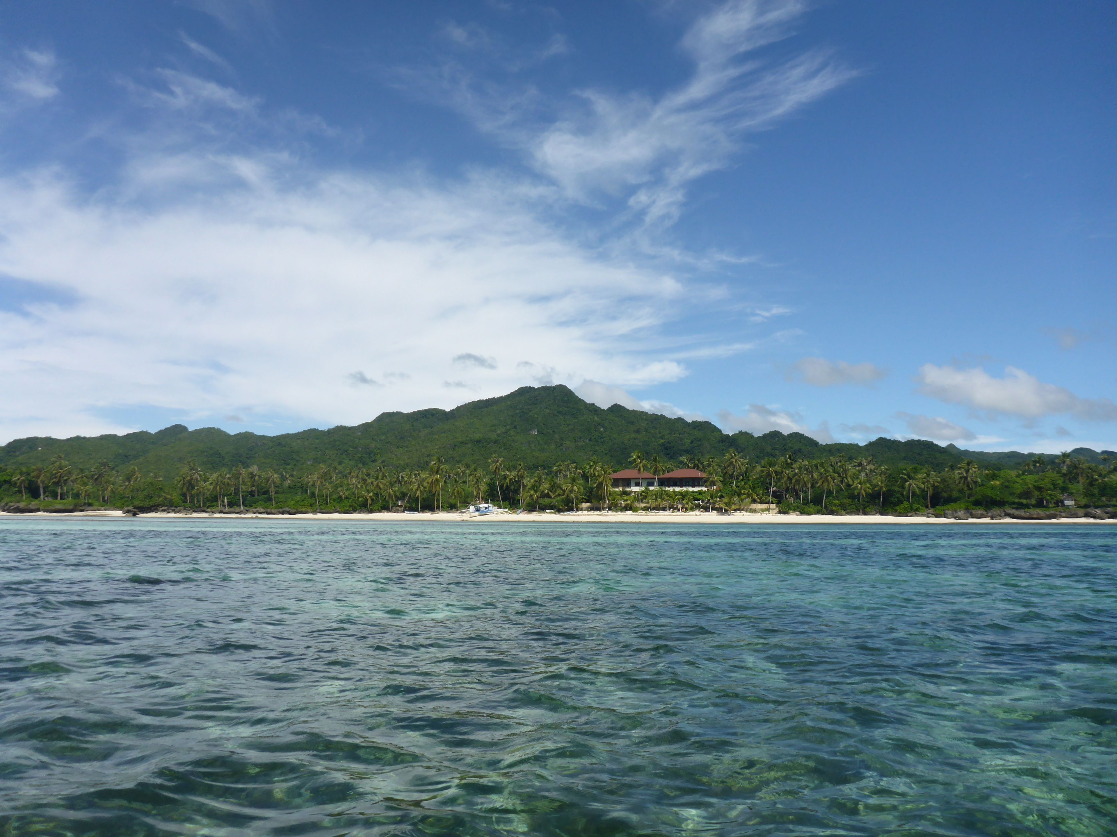 A coastal view with clear water, a sandy beach, and a mountain in the background.