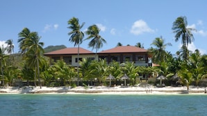 A beachfront hotel with a red roof, palm trees, and a sandy beach.