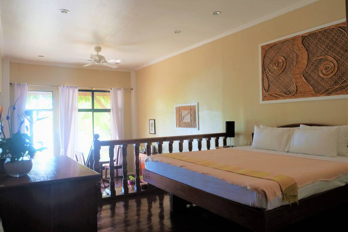Habitación de hotel con cama, escritorio, silla, ventilador de techo y ventana con cortinas.