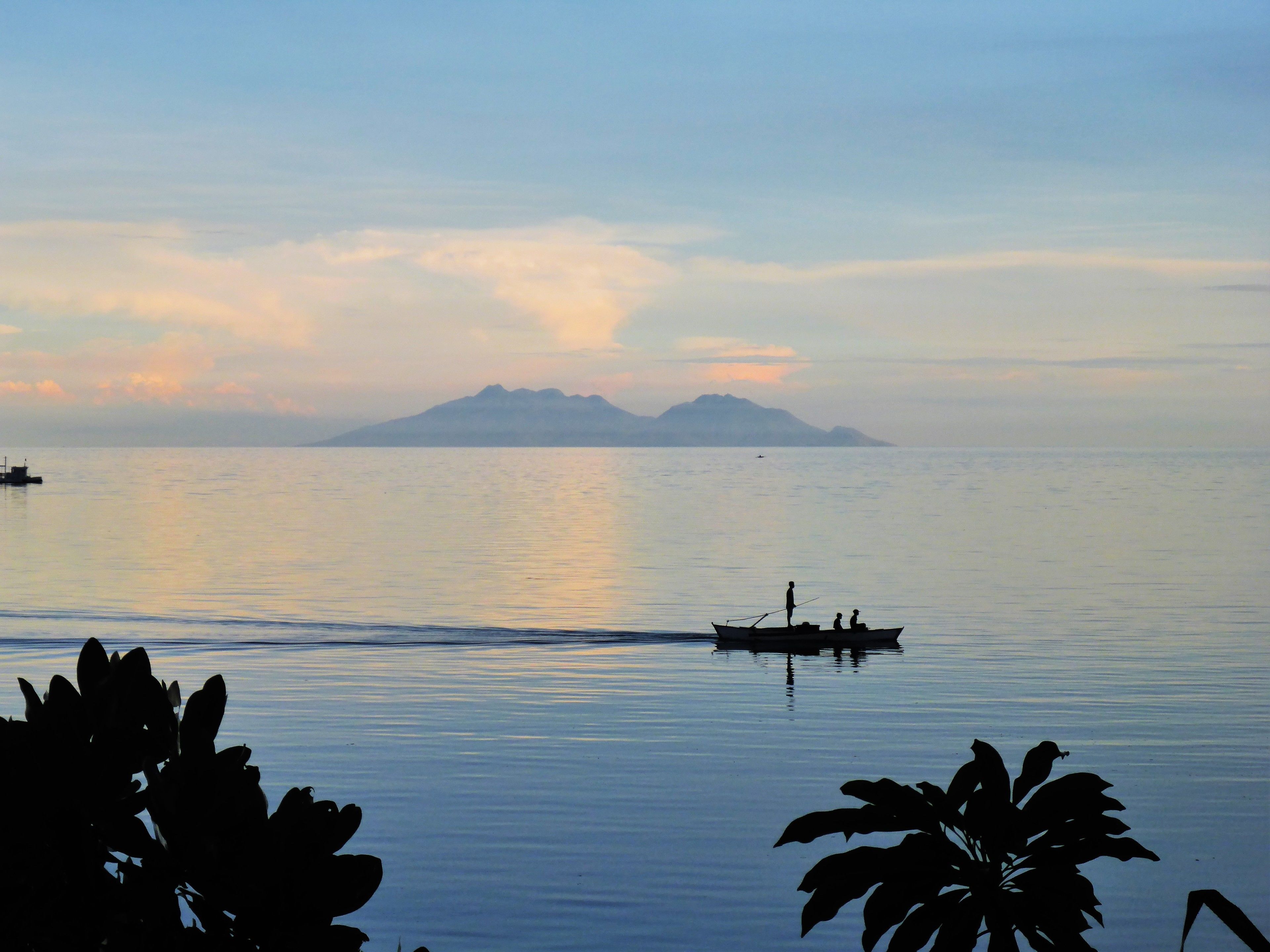 A calm body of water with a boat carrying people, a distant mountain, and a small island.