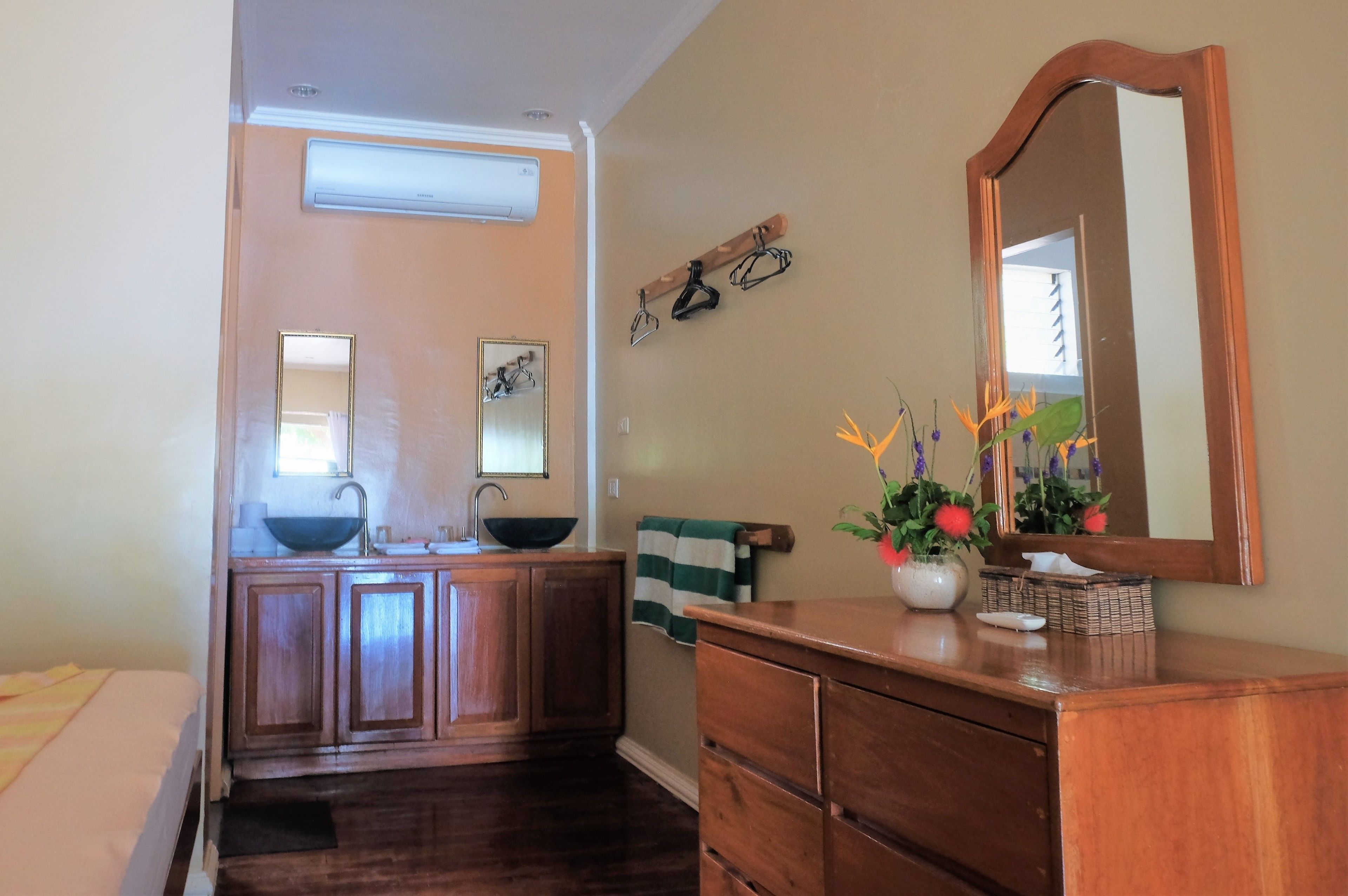 A bathroom with a wooden vanity, a sink, and a mirror. There is a towel rack with a towel and a small plant on the vanity.