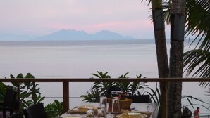 A dining table set with plates, glasses, and napkins, overlooking a body of water with mountains in the distance.