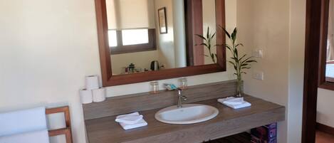 A bathroom with a wooden vanity, a white sink, and a mirror. There are towels and a potted plant on the vanity.