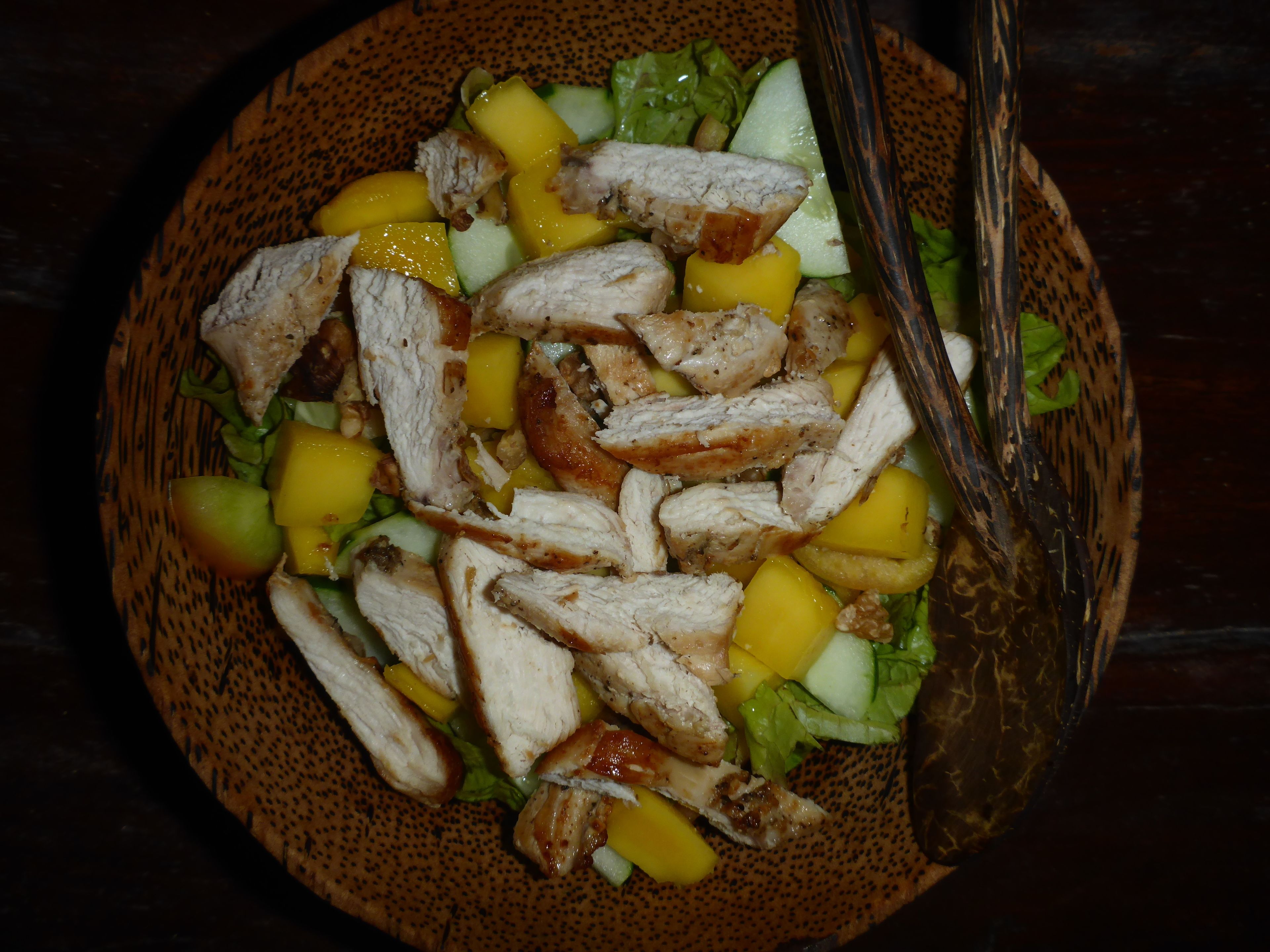 A bowl of salad with chicken, mango, and lettuce.