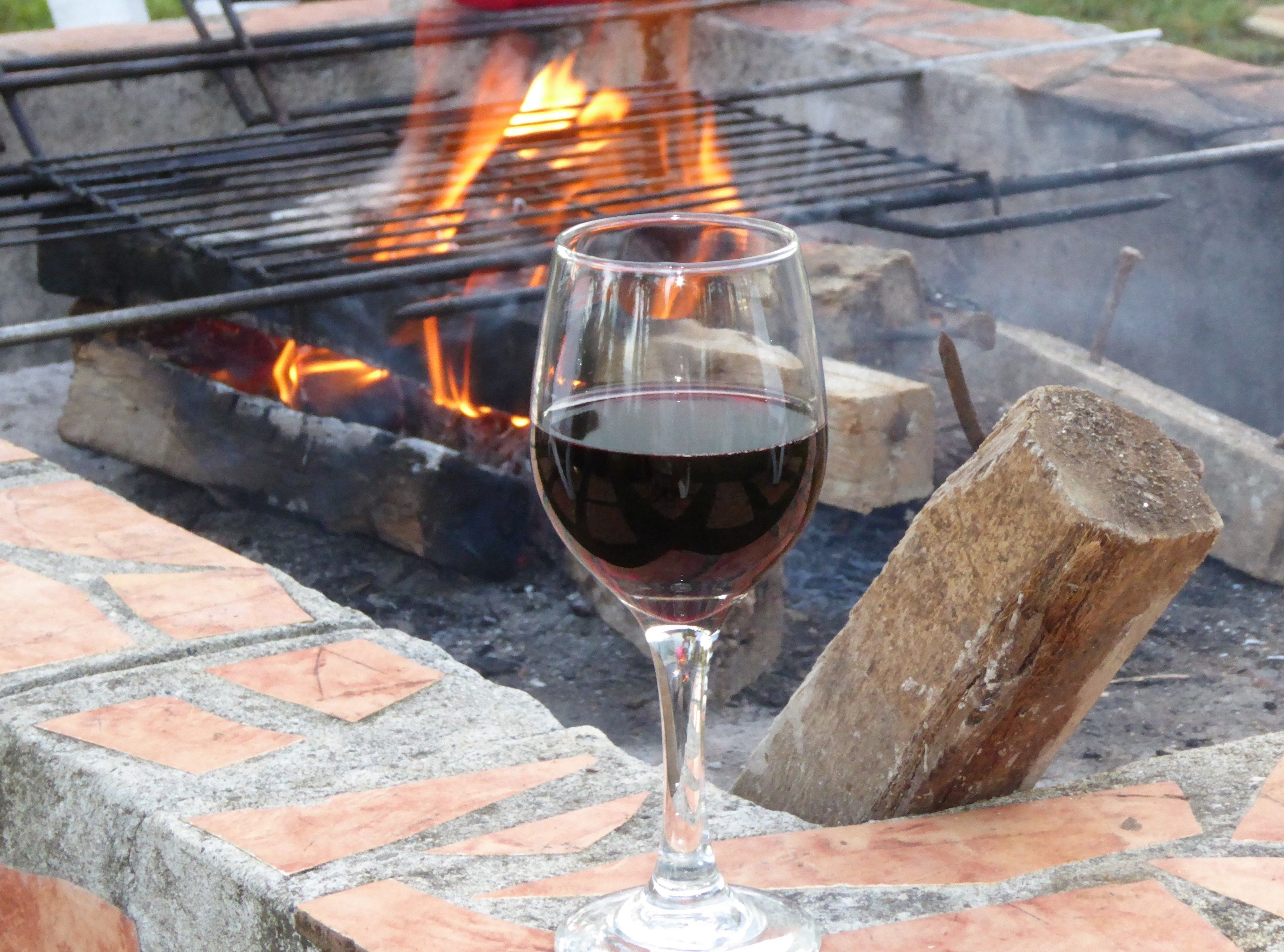A glass of red wine on a brick surface near a fire pit.