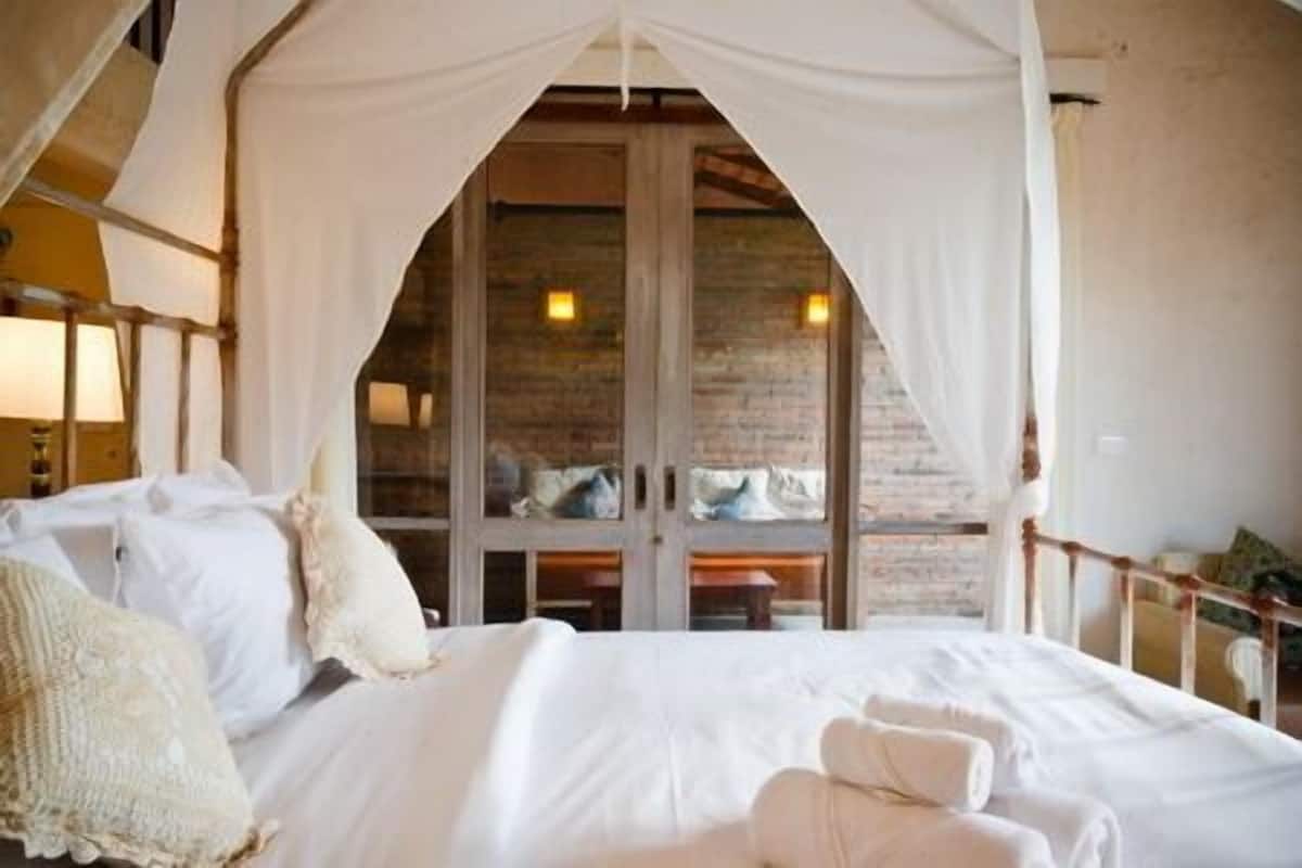 A bedroom with a canopy bed, a brick wall, and a view of a balcony.
