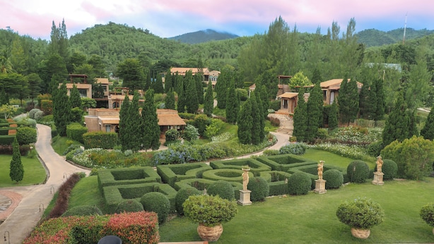 A lush garden with a winding path, manicured hedges, and a pool area with outdoor seating. - La Toscana Resort (Suan Phueng)