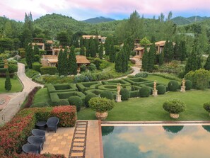 A lush garden with a winding path, manicured hedges, and a pool area with outdoor seating. - La Toscana Resort (Suan Phueng)