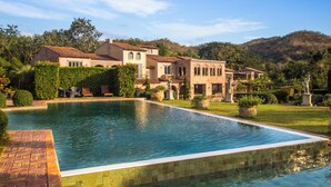 A large rectangular swimming pool with a tiled edge, surrounded by a well-maintained lawn and various plants. - La Toscana Resort (Suan Phueng)