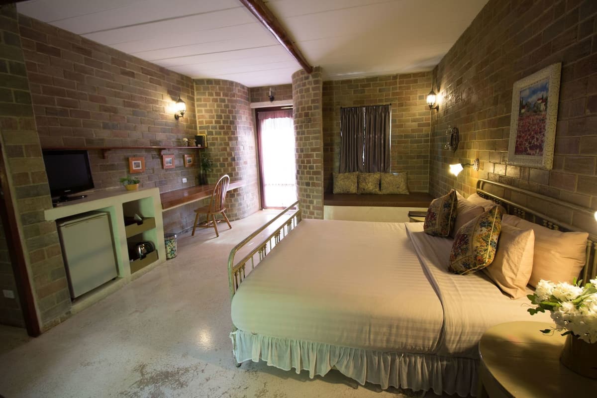 A bedroom with a bed, a television, a desk, and a window with curtains.
