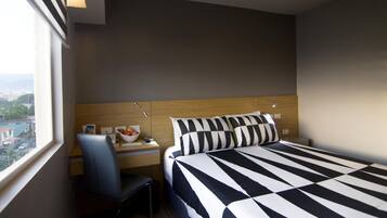 Habitación de hotel con cama, escritorio, silla y ventana con vista a la ciudad.