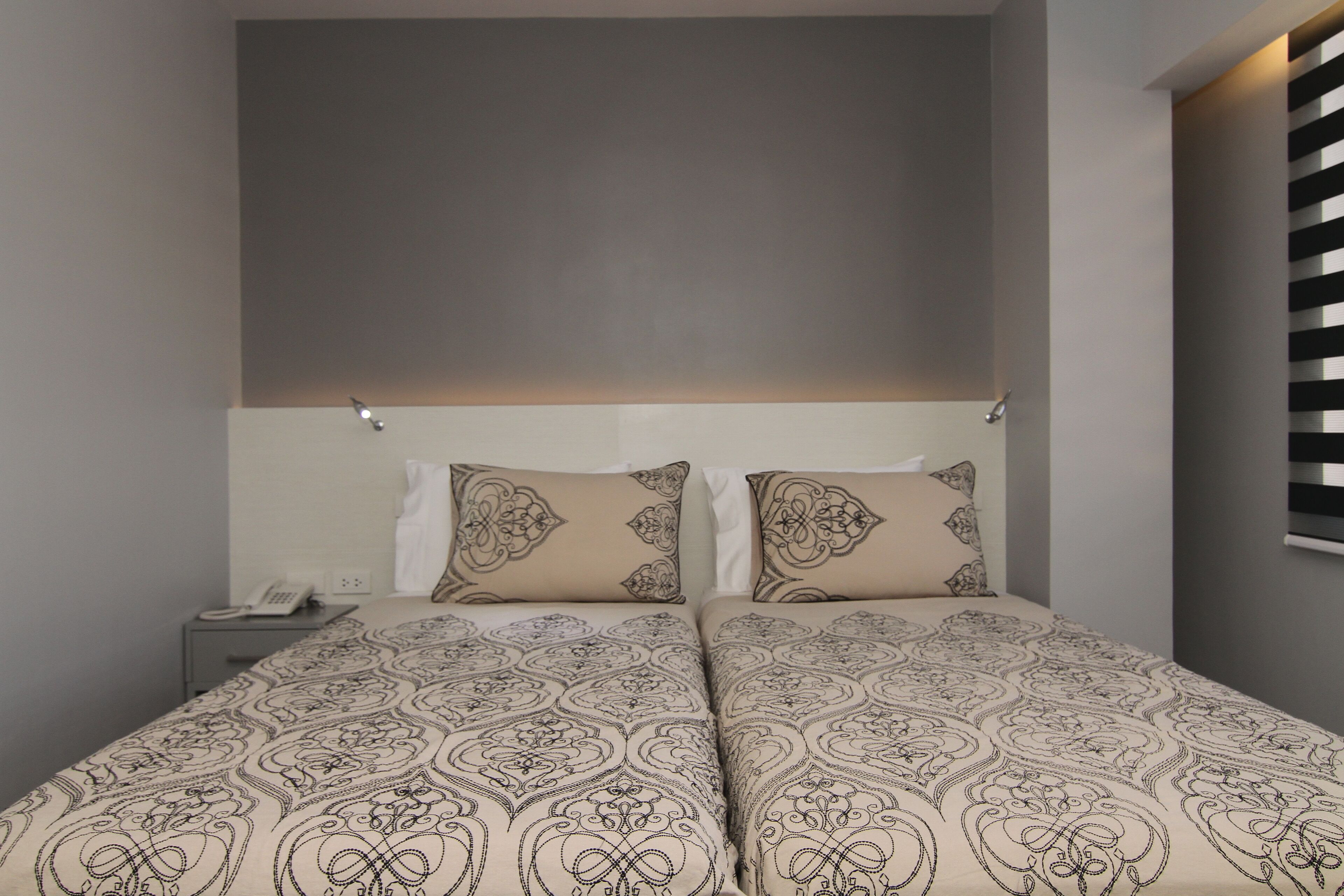 A double bed with patterned bedding, a bedside table with a phone, and a wall-mounted light fixture.