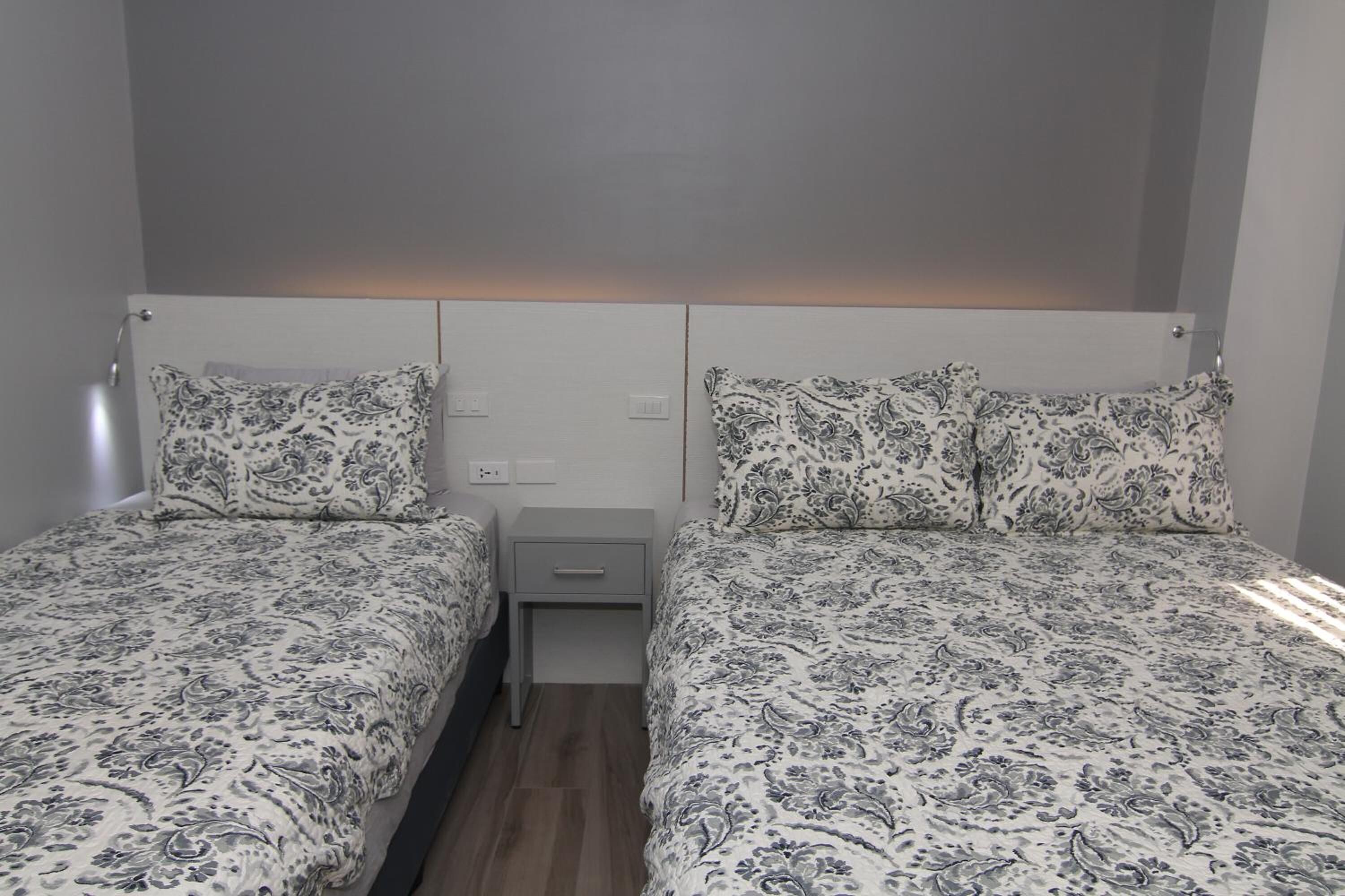 A bedroom with two beds, each with matching patterned bedding, a small bedside table, and a nightstand.