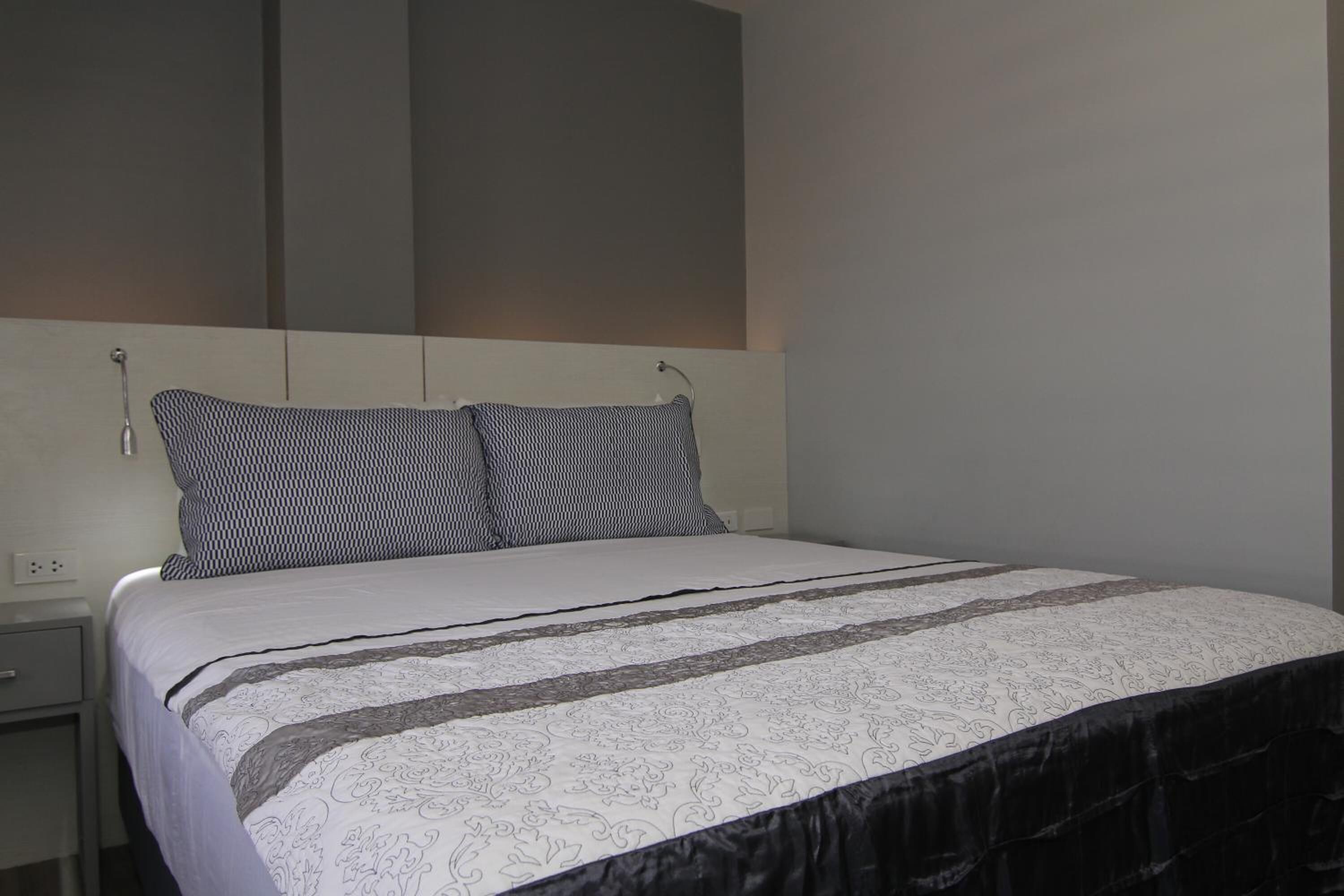 A neatly made bed with patterned bedding, a bedside table, and a wall-mounted light fixture.