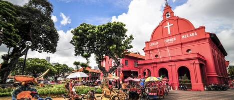 A red church with a cross on the dome, surrounded by trees and parked bicycles.