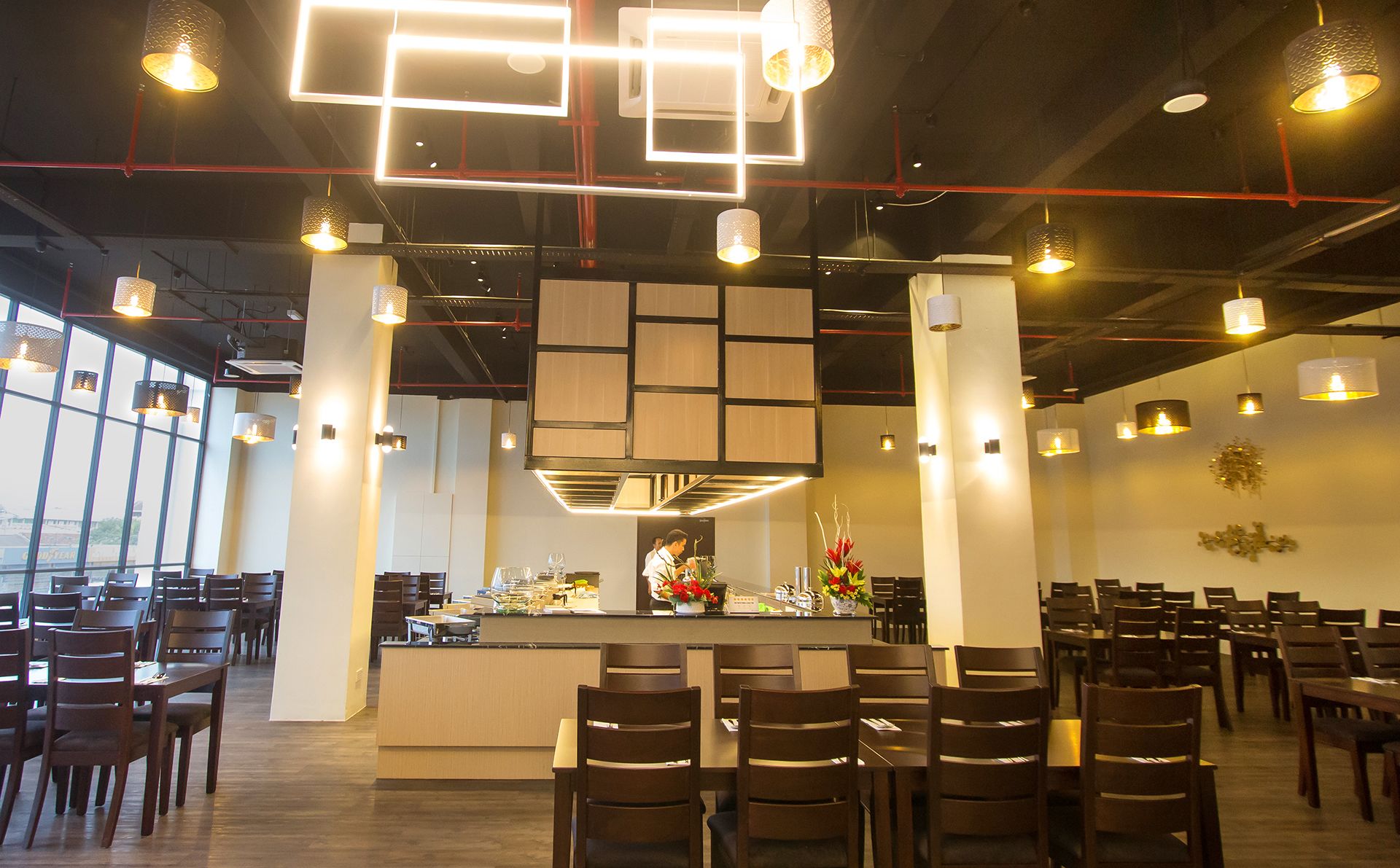 Un intérieur de restaurant moderne, caractérisé par de hauts plafonds, des luminaires suspendus et un bar central.