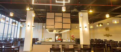 Un intérieur de restaurant moderne, caractérisé par de hauts plafonds, des luminaires suspendus et un bar central.