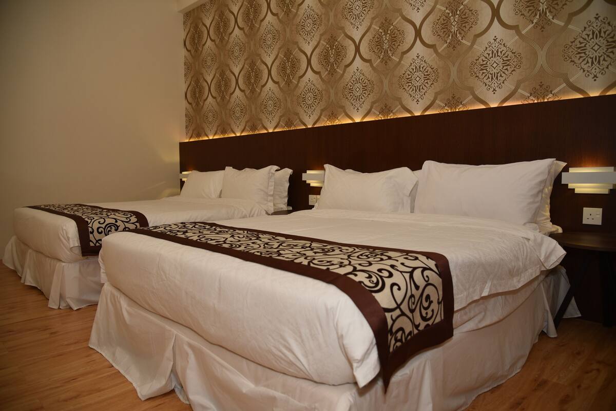 A hotel room with two beds, each with white linens and a decorative headboard.