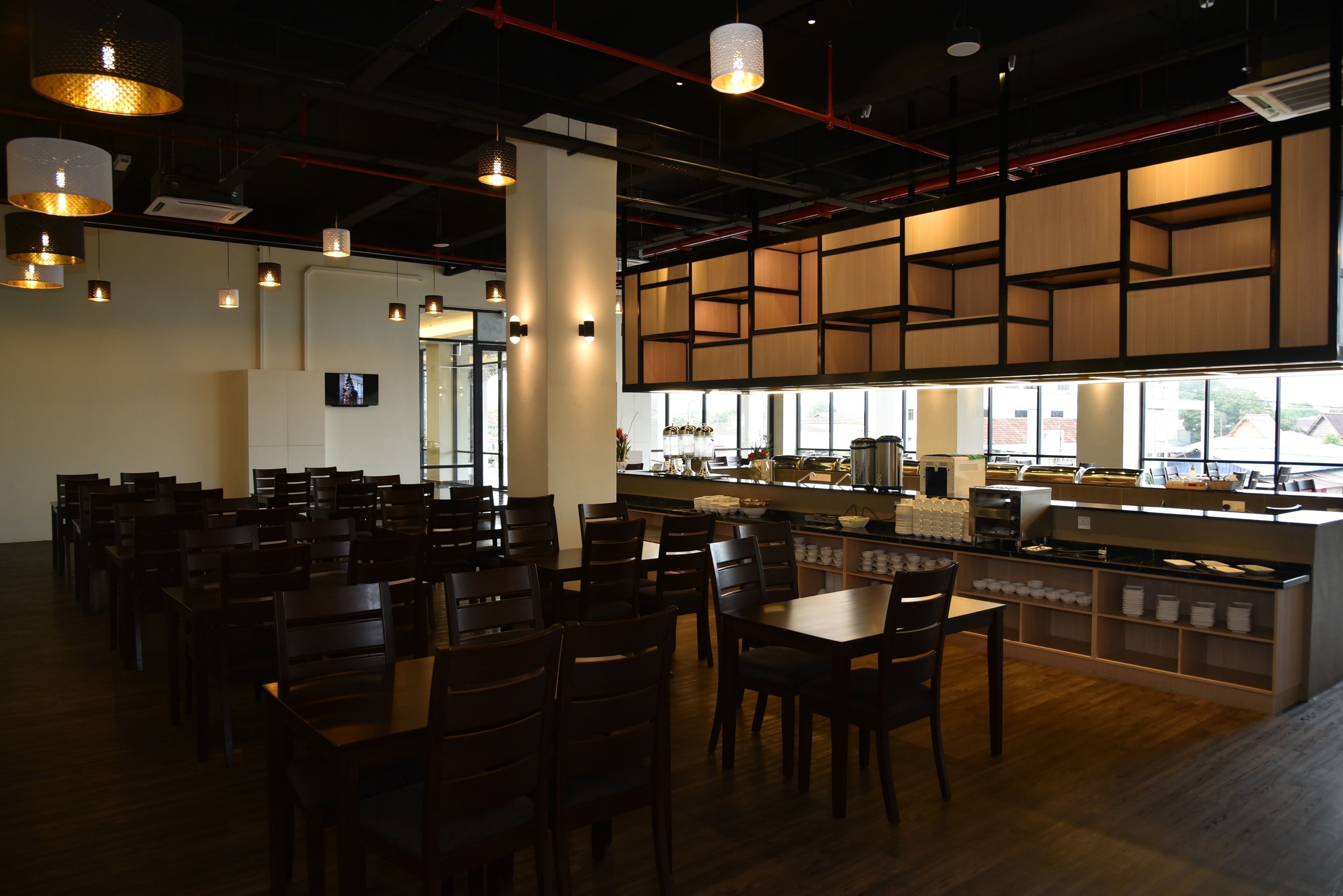 A restaurant with wooden tables and chairs, a counter with food display, and hanging pendant lights.