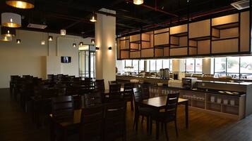 A restaurant with wooden tables and chairs, a counter with food display, and hanging pendant lights.