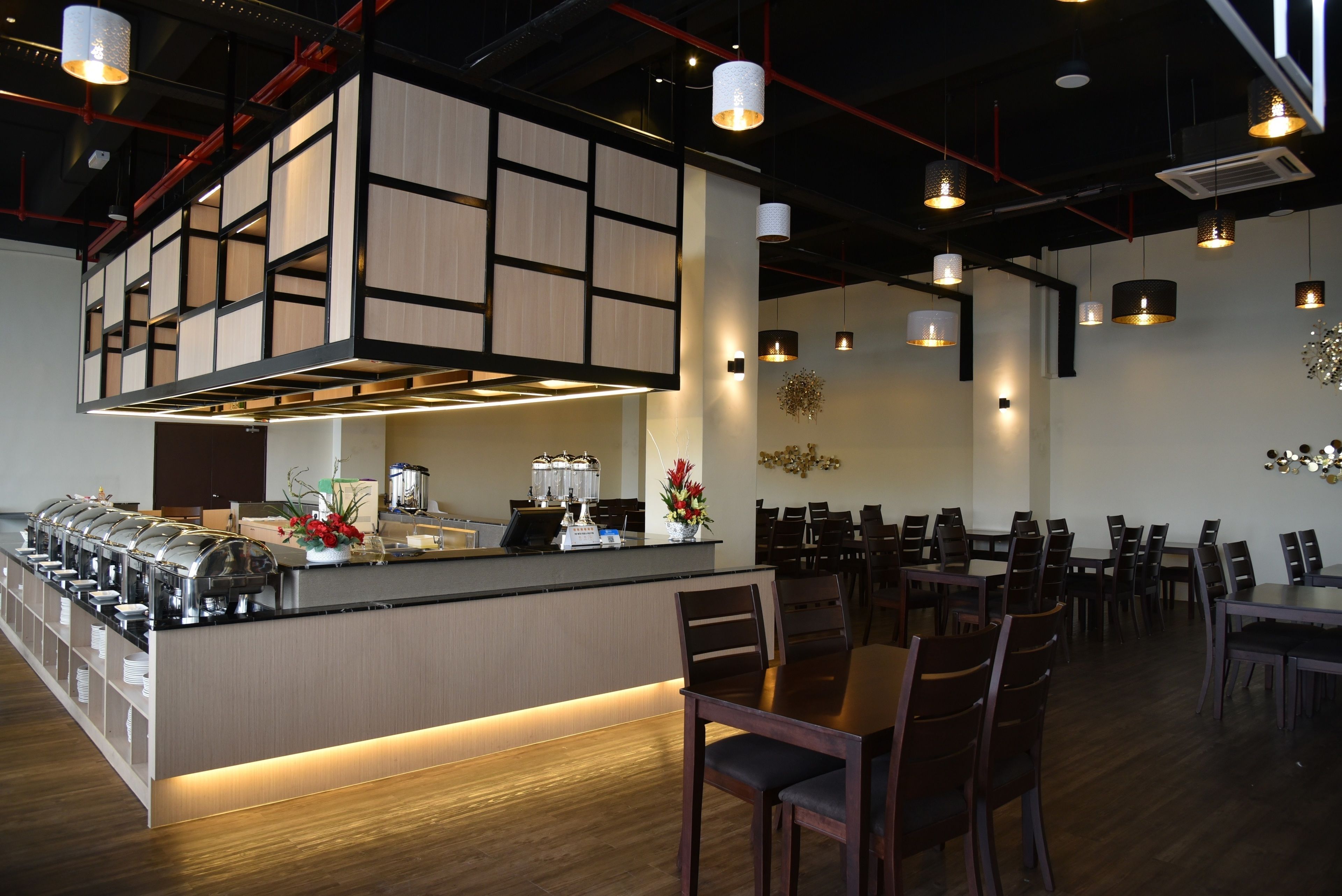 A modern restaurant with a buffet counter, wooden flooring, and contemporary lighting fixtures.