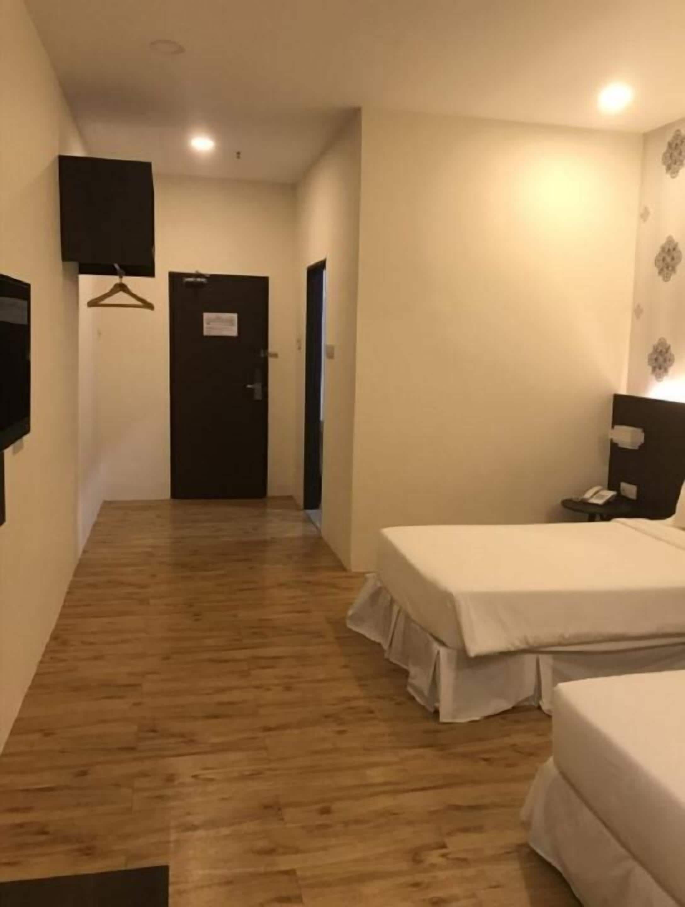 Une chambre d’hôtel avec un plancher en bois, deux lits simples, un bureau avec une chaise, un téléviseur fixé au mur et une porte avec une pancarte.
