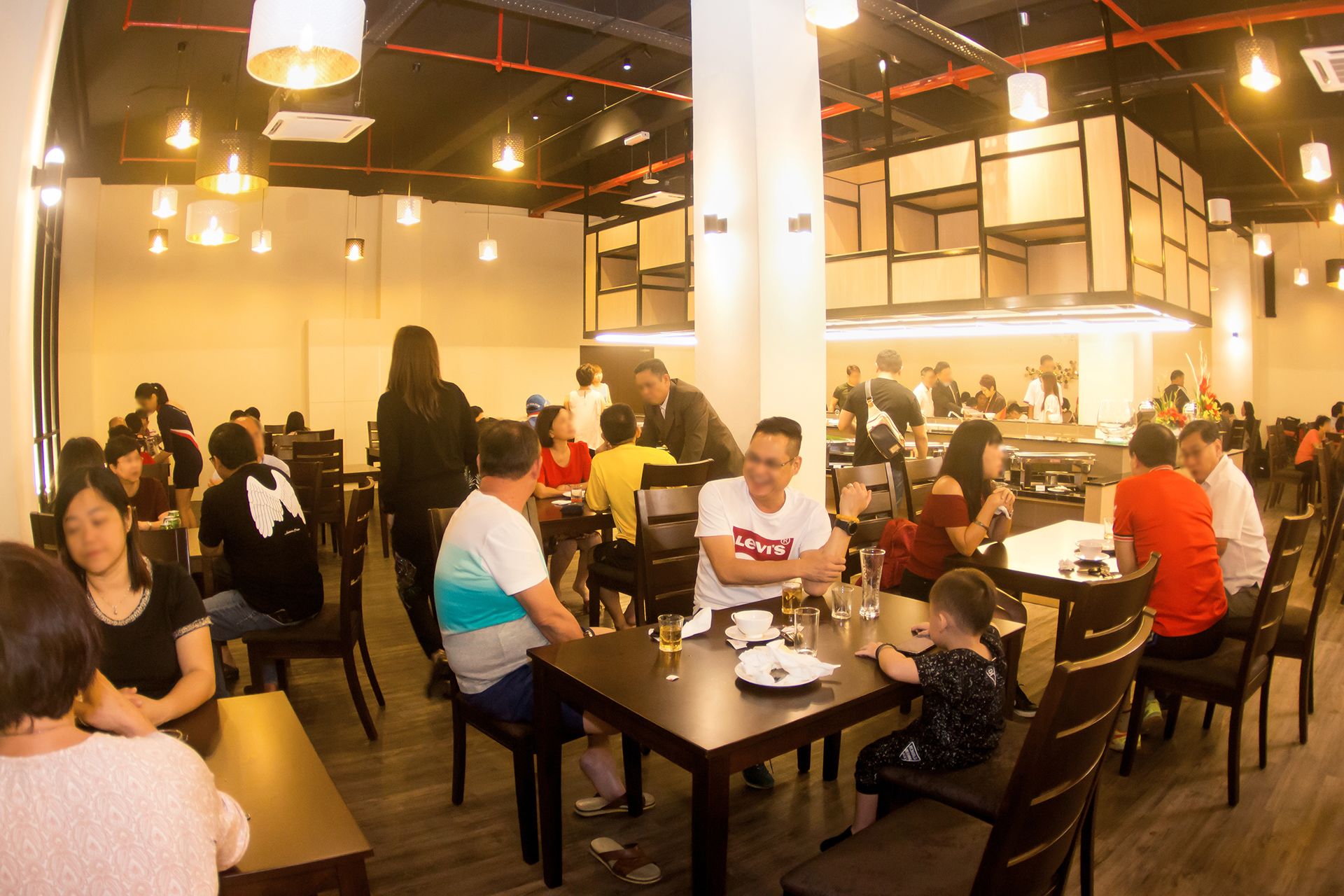 A busy restaurant with multiple tables and chairs, a counter area, and hanging lights.