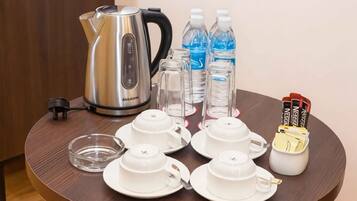 A table with a kettle, water bottles, cups, a glass, and a small container with items.