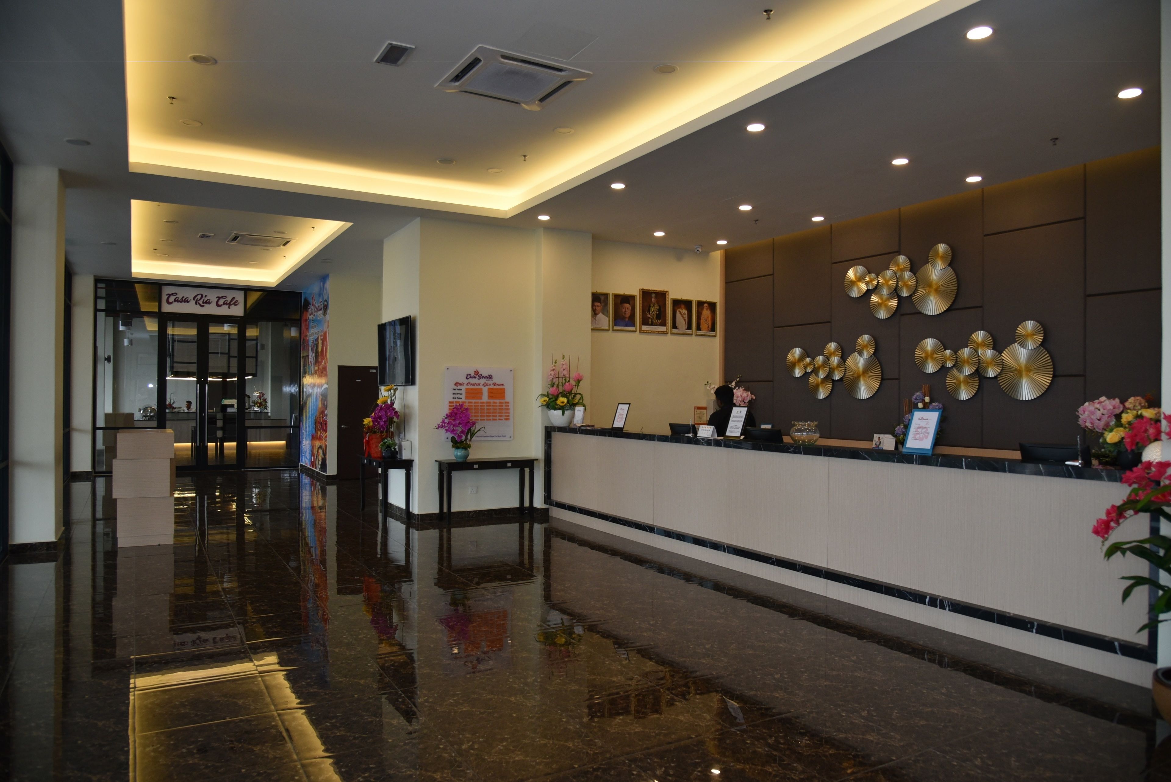 Zona de recepción de hotel con piso de mármol pulido, una mesa de recepción y una pared decorada con cuadros y elementos decorativos.