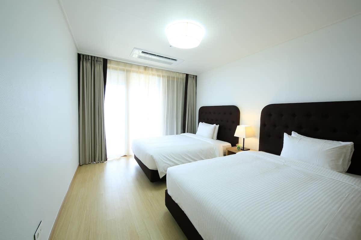 Une chambre d’hôtel avec deux lits, un luminaire au plafond, un appareil de climatisation et une fenêtre avec des rideaux.