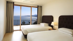 A hotel room with two beds, a large window with a view of the sea, and a ceiling light. - Jeju Booyoung Resort (Seogwipo)