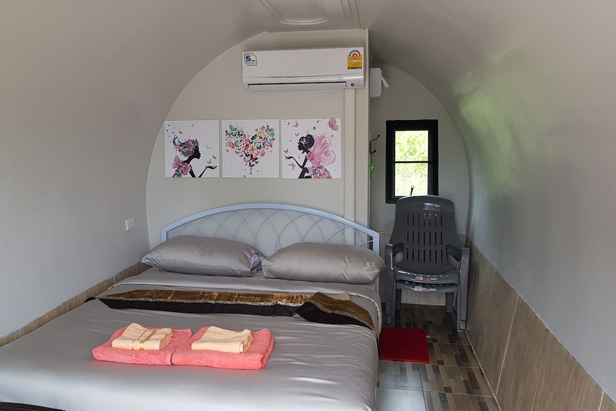 Un dormitorio pequeño con cama, almohadas, una silla y decoración en la pared.