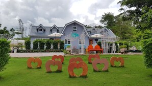 Un bâtiment à la façade bleue, un jardin orné de sculptures en forme de cœur et un espace de jeux avec des chaises orange.
