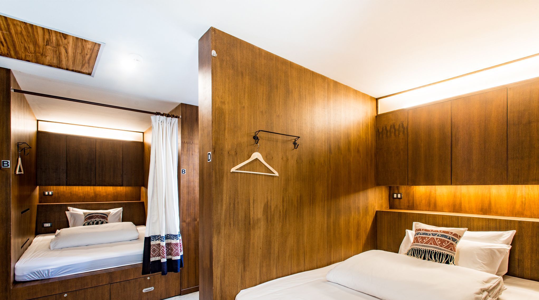 A hotel room with a wooden headboard, a bed with white bedding, a hanging coat rack, and a mirror reflecting part of the room.