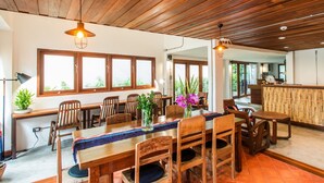 A dining area with wooden tables and chairs, large windows, and a bamboo partition. - Baan Heart Thai - Hostel (Chiang Mai)