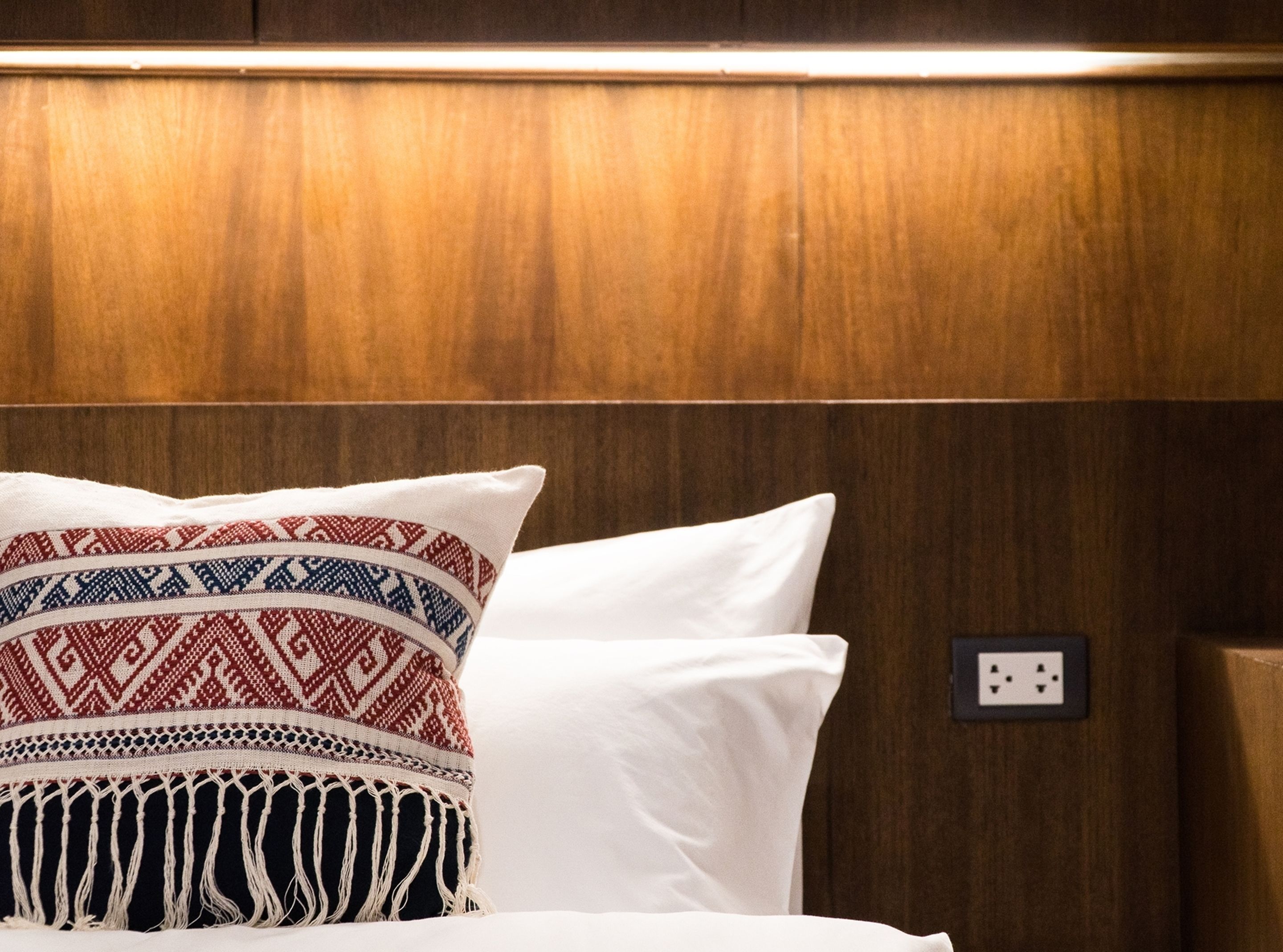 A bed with patterned pillows and a plain white pillow against a wooden headboard.