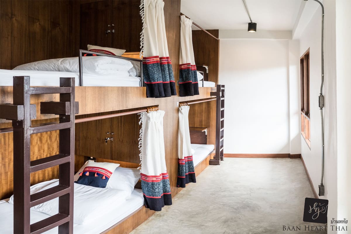 Een slaapzaal met stapelbedden, houten hoofdborden en een simpel, net design.